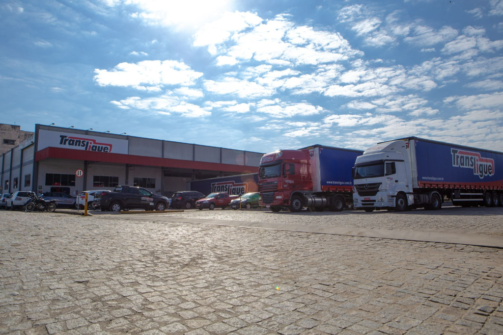 Unidade da Transligue com caminhões da frota em operação de transporte rodoviário de cargas, estacionados em frente ao centro logístico